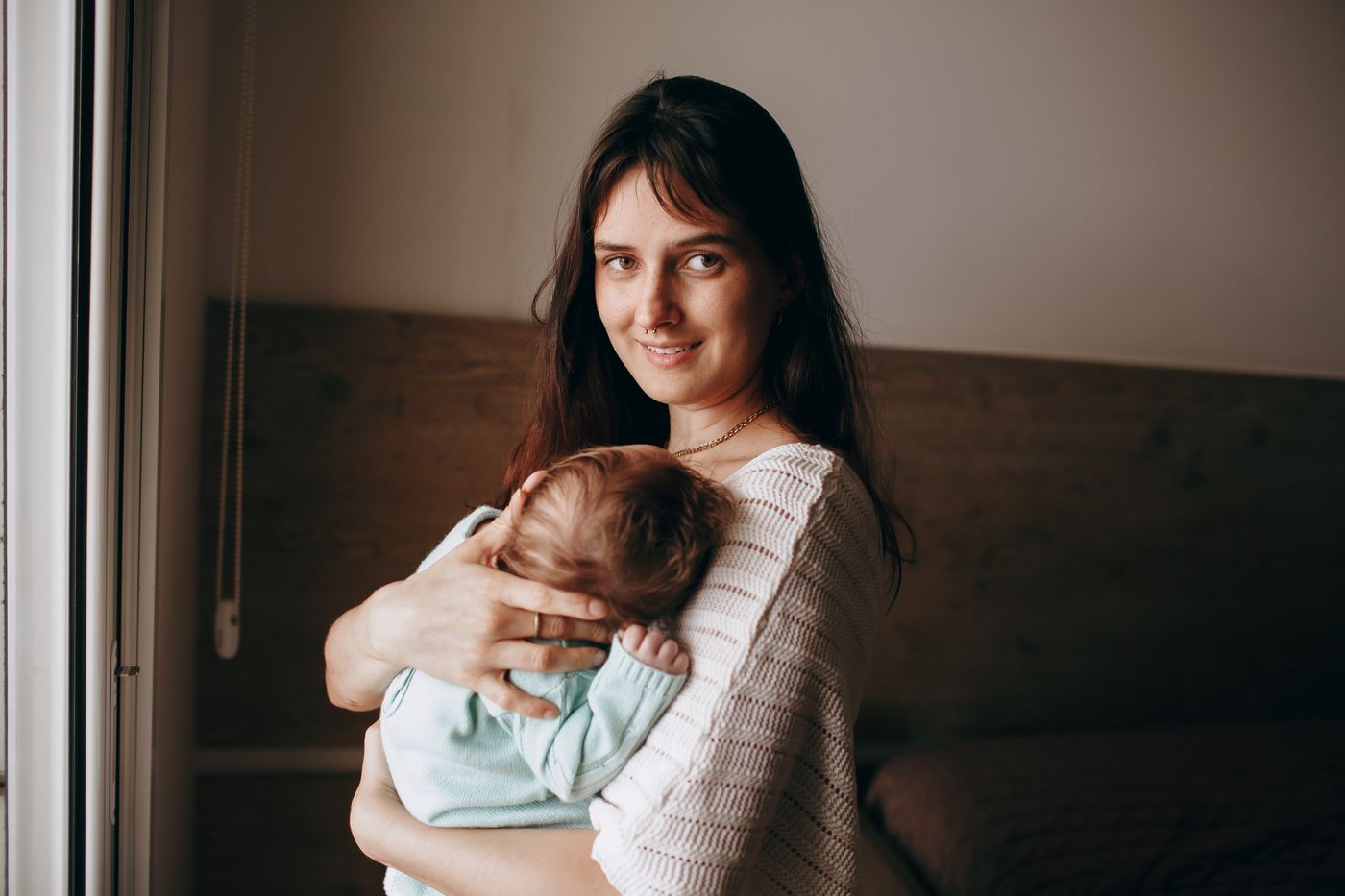 A mother holding her newborn by a window in warm light